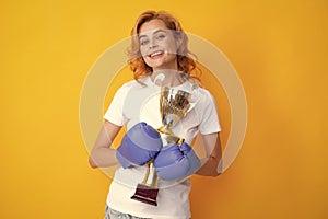 Woman in boxing gloves hold champion winner cup trophy. Winner female boxer Isolated on yellow background. Winning