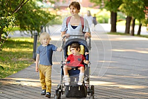 Woman with a boy and a disabled girl in wheelchair walking in park summer. On baby legs orthosis. Child cerebral palsy. Treatment photo
