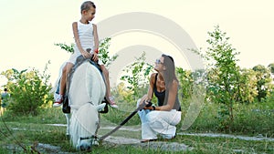 A woman and a boy are walking around the field, son is riding a pony, mother is holding a pony for a bridle. Cheerful