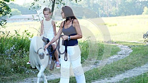 A woman and a boy are walking around the field, son is riding a pony, mother is holding a pony for a bridle. Cheerful