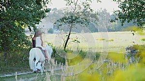 A woman and a boy are walking around the field, son is riding a pony, mother is holding a pony for a bridle. Cheerful