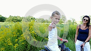 A woman and a boy are walking around the field, son is riding a pony, mother is holding a pony for a bridle. Cheerful