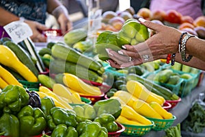 Woman with bracelets on holds two green peppers to buy at a farmer`s market