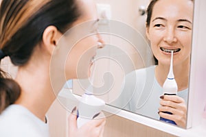 Woman with braces on her teeth brushing her teeth with by using a irrigate, before mirror.