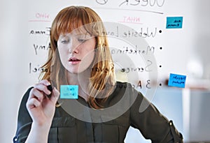 Woman, brainstorming or writing ideas on glass board and sticky note planning in office with paper. Creative project