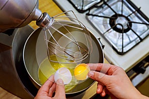 Woman breaks an egg in a metal bowl. Separate white from yolk.