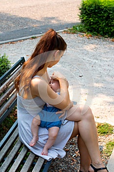 Woman breastfeeding baby outdoor in public, gently covering and protecting her child from sun
