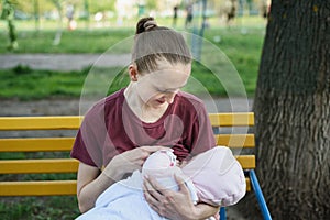 Woman is breastfeeding a baby in a park on a bench. Spring day
