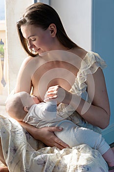 A woman breastfeeds a baby sitting on the floor