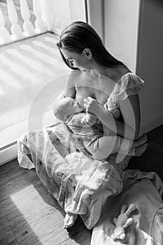 A woman breastfeeds a baby sitting on the floor