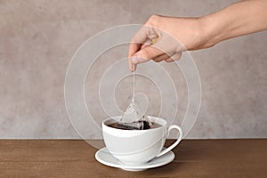 Woman brewing tea with bag in cup on table