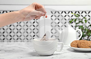 Woman brewing tea with bag in cup on table