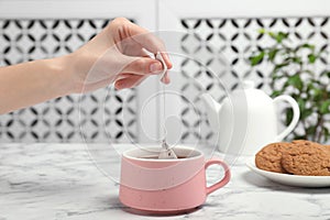 Woman brewing tea with bag in cup on table