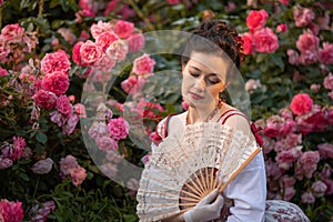 Woman bride in a ancient vintage historical dress posing in the beautiful summer rose garden