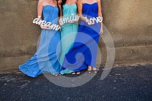 Woman bride maids in colorful blue dresses hold up a sign. Smile, love and dream