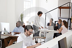 Woman briefing colleagues around a desk in open plan office