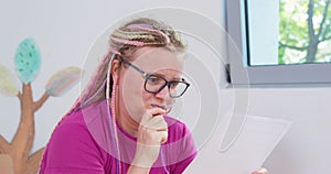 Woman bright braids glasses sits look sheet nervous biting hair panicking exam