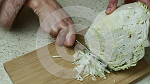 A woman on a bright kitchen table deftly finely chop white cabbage on a cutting board with a sharp kitchen knife