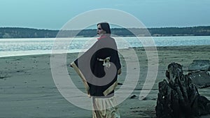 A woman with bright makeup in a traditional kimono dances on the riverbank. Strange hand movements.