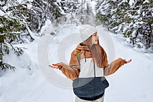 woman with bright red hair enjoying the snowfall in winter forest, walking alone