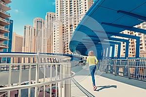 Woman in bright sportswear quickly runs across a pedestrian bridge in the Dubai Marina district. The concept of a female