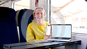 woman in bright yellow clothes in the train wagon near the table first class seat in hands phone on the table laptop