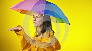 woman in bright yellow raincoat with a rainbow umbrella is checking for the rain