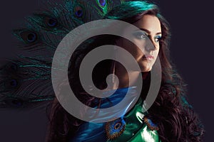 Woman in brilliant blue dress with peacock feathers design. Creative fantasy makeup, long dark hair fluttering at wind.