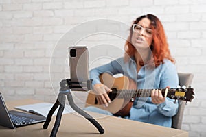 A woman is broadcasting online on her phone at home. The girl sings and plays the guitar live