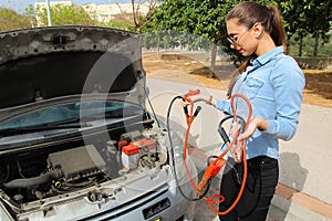 A woman with a broken car, hole cables waits for assistance