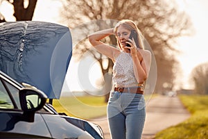 Woman With Broken Down Car On Country Road Calling For Help On Mobile Phone