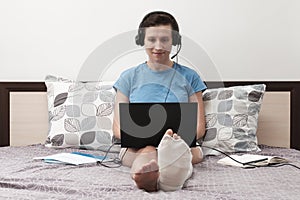 A woman with a broken leg works from home. A woman with headphones is sitting on the bed and holding a laptop on her lap