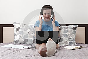 A woman with a broken leg works from home. A woman with headphones is sitting on the bed and holding a laptop on her lap