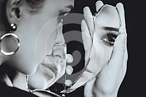 Woman with broken self-image mirror on black background, black and white portrait