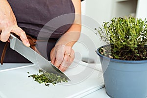 woman in brown apron cuts herbs on cutting board with sharp kitchen knife