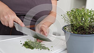 woman in brown apron cuts herbs on cutting board with sharp kitchen knife