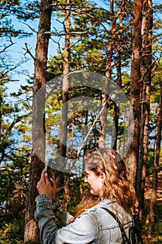 Woman with brown curly hair hiking and taking pictures with phone of the seaside by the Panga cliff forest in Saaremaa, Estonia