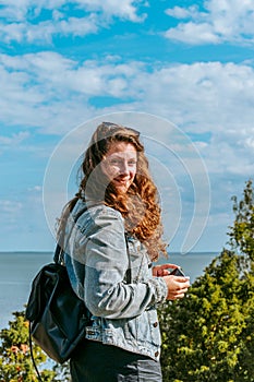 Woman with brown curly hair hiking and taking pictures with phone on the seaside by the Uugu cliff on the Muhu Island near