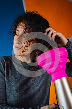 Woman with brown curly hair holding a blow dryer with the other hand