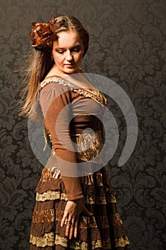 Woman in a brown dress standing beside a wall.