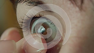 Woman with brown eyes putting on a soft contact lens on her eye, close-up