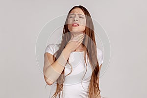 Woman with brown hair standing touching neck, frowning from pain, suffering sore throat, flu symptom