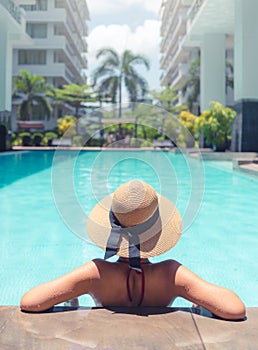 Woman with brown hat relaxing in swimming pool with blue water in sun , holiday concept