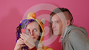 Woman browsing mobile phone on pink background. Man peeping in female's smartphone. Woman looks at male, he turns