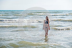 Woman bruenette with long hair in blue bikini going to swim in the wave`s sea. Front view. Close-up