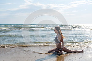 Woman bruenette with long hairs in blue bikini is stretching on the seashore. Side view.