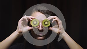 Woman brunette girl holding a kiwi fruit on their eyes against a dark background