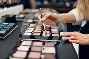 Woman with brush choosing shadows, cosmetics store