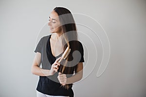 Woman brushes her long hair with wooden hairbrush