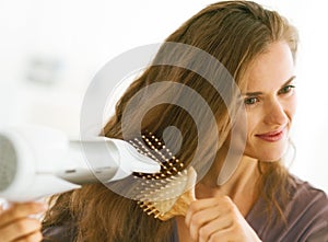 Woman brushing and blow drying hair in bathroom